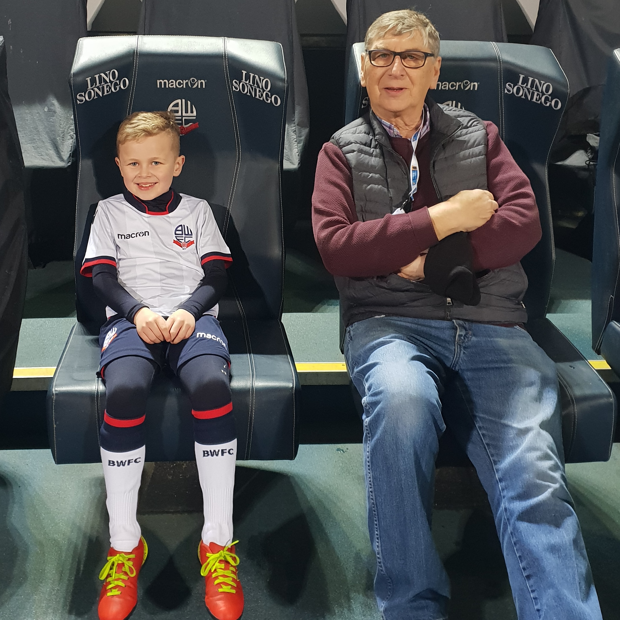 Young boy wearing a Bolton Wanderers kit, sat next to an elderly man.