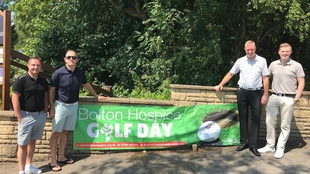 Four men stood either side of a large green 'Golf Day' banner