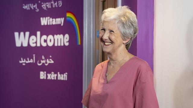 Woman wearing pink scrubs stood next to Welcome sign.